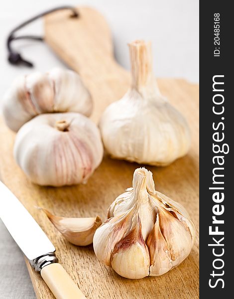 Four garlic bulbs on a chopping board with a knife. Four garlic bulbs on a chopping board with a knife