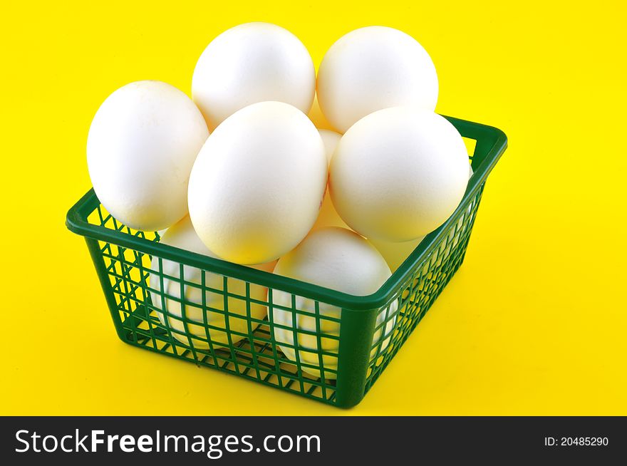 White eggs are in a plastic basket against a yellow background. White eggs are in a plastic basket against a yellow background