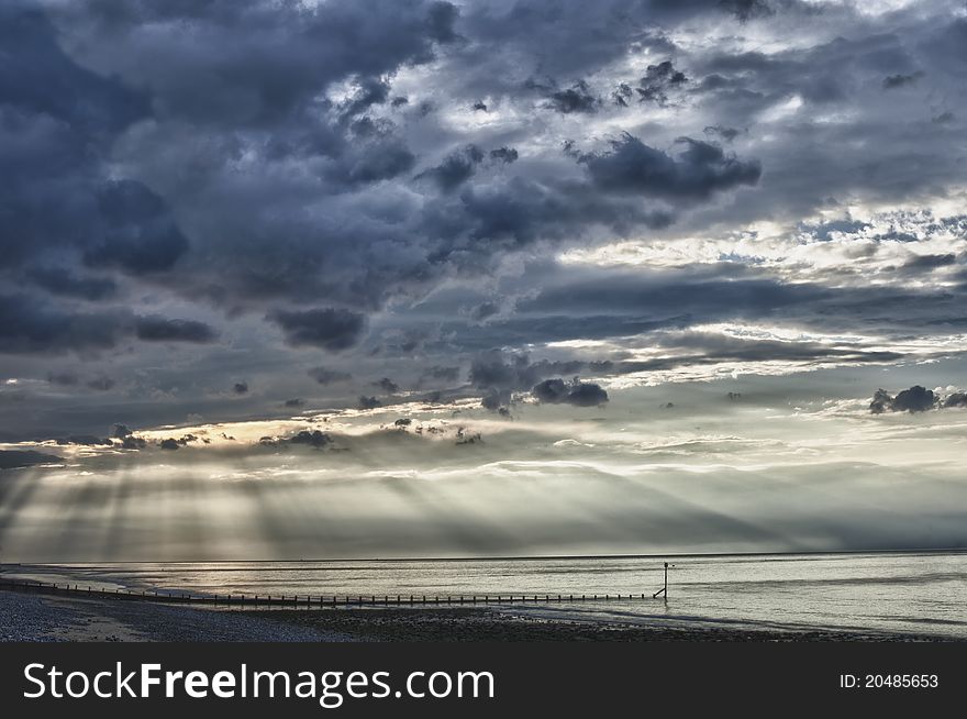 Suns rays bursting through clouds on sea, at near sunset. Breakwater and beach in foreground. HDR image. Suns rays bursting through clouds on sea, at near sunset. Breakwater and beach in foreground. HDR image