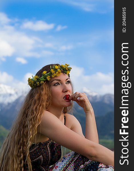 Girl in wreaths of dandelions with long hair, eats red berry on the nature. Girl in wreaths of dandelions with long hair, eats red berry on the nature