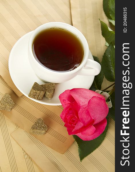 White cup of tea next to sugar and is a beautiful red rose lying on sheets of old paper sheet music. White cup of tea next to sugar and is a beautiful red rose lying on sheets of old paper sheet music