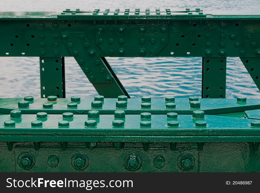 Construction of old green bridge, with lots of bolts and screws. Sea in background