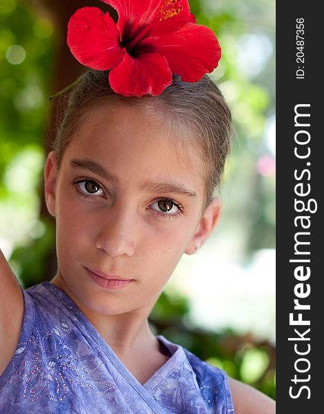 Head and shoulders outdoor summer portrait of 8 years girl wearing red flower of hibiscus in her hair. Head and shoulders outdoor summer portrait of 8 years girl wearing red flower of hibiscus in her hair
