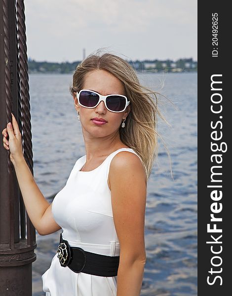 Beautiful blond girl in white dress near the river in summer day