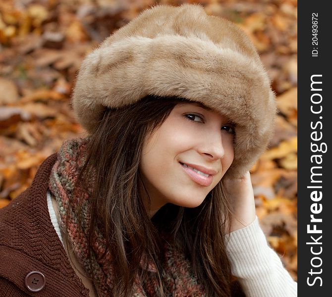 A close-up portrait of a beautiful young woman in a fuzzy hat and scarf, enjoying fall weather with leaves behind her. A close-up portrait of a beautiful young woman in a fuzzy hat and scarf, enjoying fall weather with leaves behind her