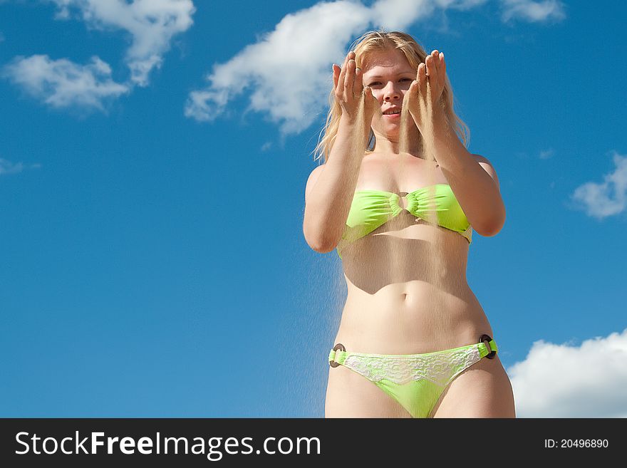 Smiling woman in bikini with sand trough fingers