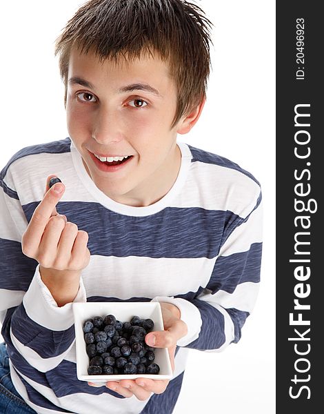 A boy holding a single blueberry in his fingers and smiling, while holding a small bowl filled with the delicious blueberries. A boy holding a single blueberry in his fingers and smiling, while holding a small bowl filled with the delicious blueberries.