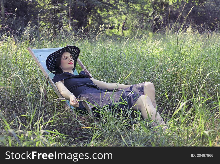 Beautiful woman relaxing on a deckchair on a green meadow