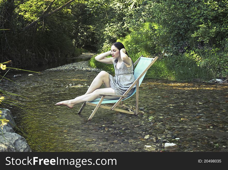 Beautiful woman on a deckchair refreshing her feet in a river