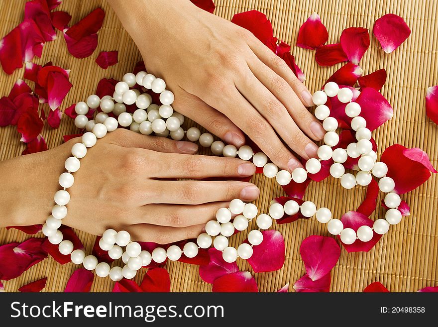 Close-up of beautiful hand braided with pearls and lie on red rose petals. Close-up of beautiful hand braided with pearls and lie on red rose petals