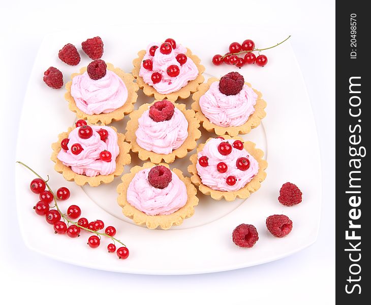 Tartlets with whipped cream, fruits and sprinkles - raspberries and redcurrants - on a plate