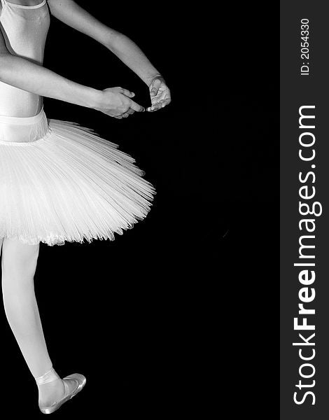 Ballerina standing in a drak black room with a white tutu