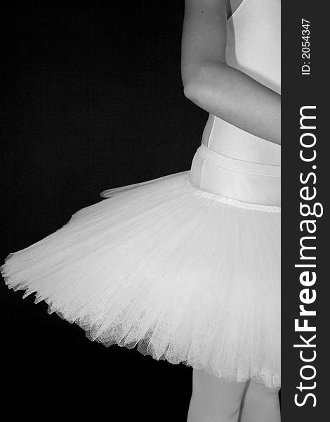 Ballerina standing in a drak black room with a white tutu