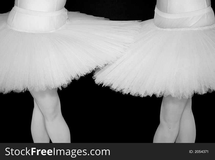 Two Ballerinas standing in a drak black room with a white tutu