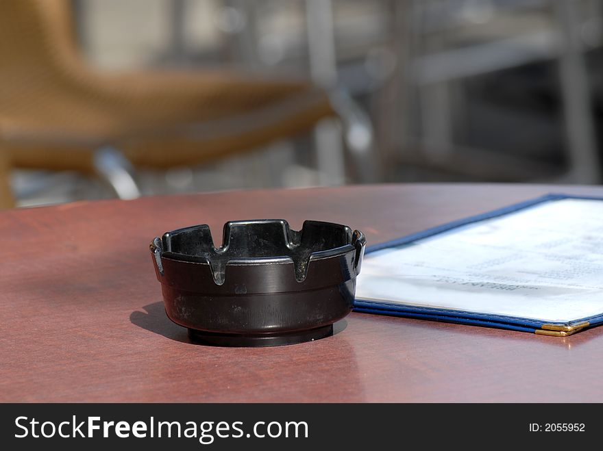 An ashtray and menu on a table in a sidewalk cafe dining area. An ashtray and menu on a table in a sidewalk cafe dining area