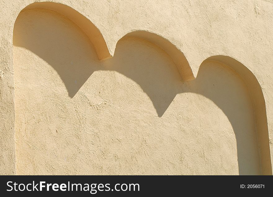 A stucco wall with three arches casting shadows