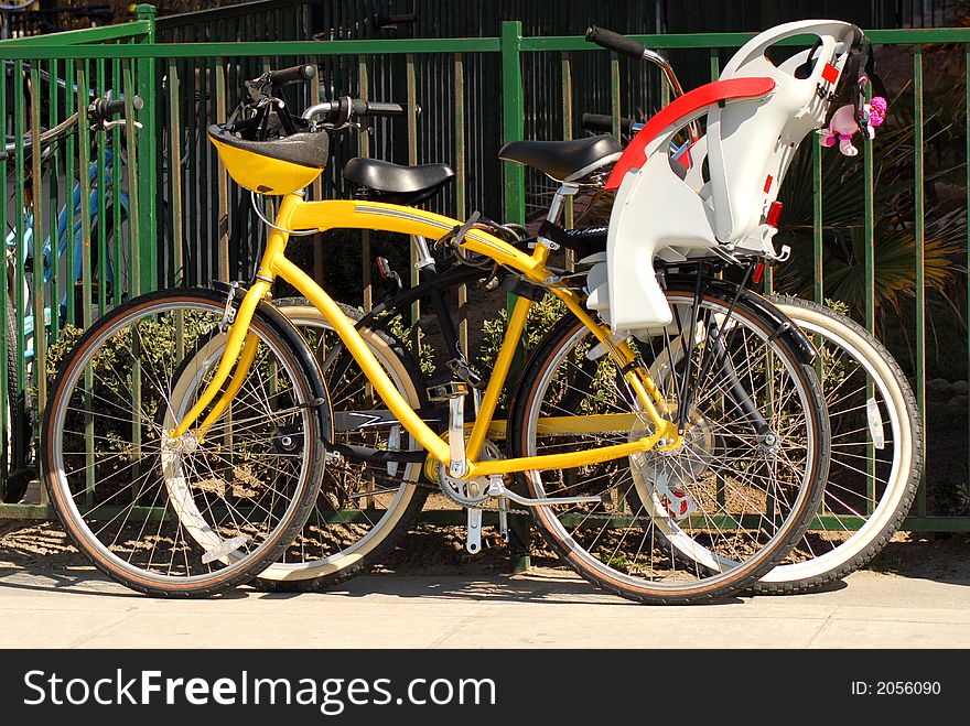 Two bicycles resting against a fence on a sidewalk