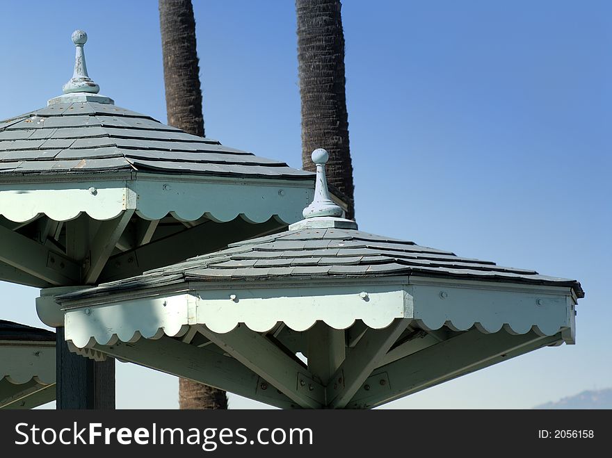 The roofs of two beach shelters in front of palm trees