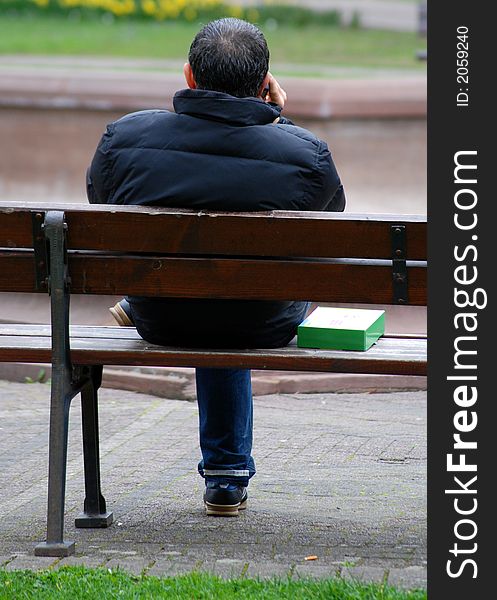 A young man is making  call in park, sitting on a bench. A young man is making  call in park, sitting on a bench.