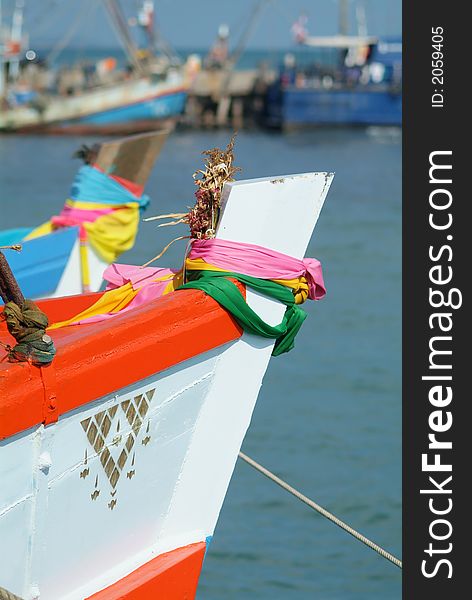 Bow of orange and white wooden fishing boat in a harbour in Rayong, Thailand. Blurred fishing boats in the background. Bow of orange and white wooden fishing boat in a harbour in Rayong, Thailand. Blurred fishing boats in the background.