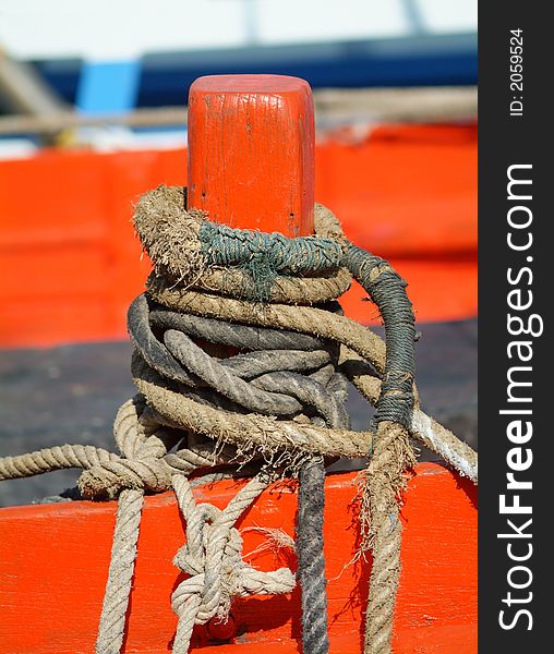 Several old, worn ropes on an orange cleat at a wooden boat.