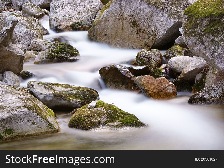 A clean stream flowing between rocks in a forest. A clean stream flowing between rocks in a forest.