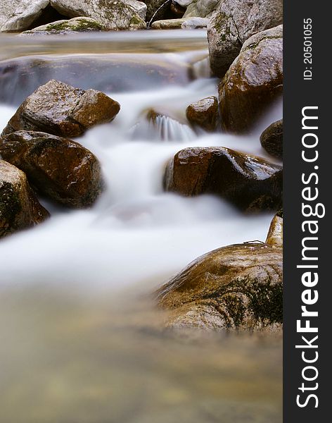 A clean stream flowing between rocks in a forest. A clean stream flowing between rocks in a forest.