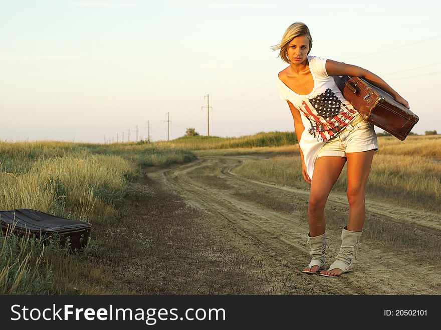 Pretty girl with a suitcase on a countryside road