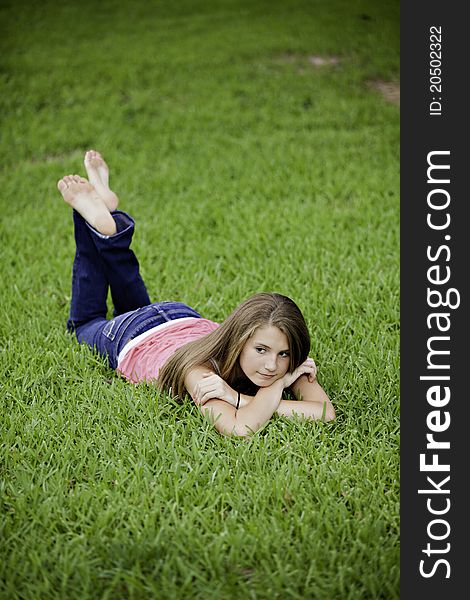 A pretty teenage female girl laying face down on green grass looking thoughtful. A pretty teenage female girl laying face down on green grass looking thoughtful.