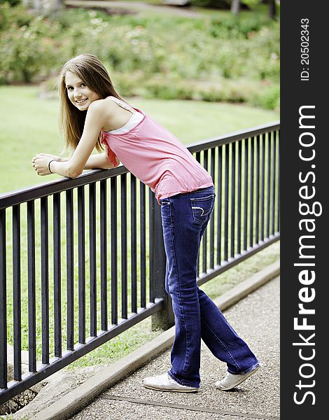 A pretty teenage female girl leaning against a rail fence smiling. A pretty teenage female girl leaning against a rail fence smiling