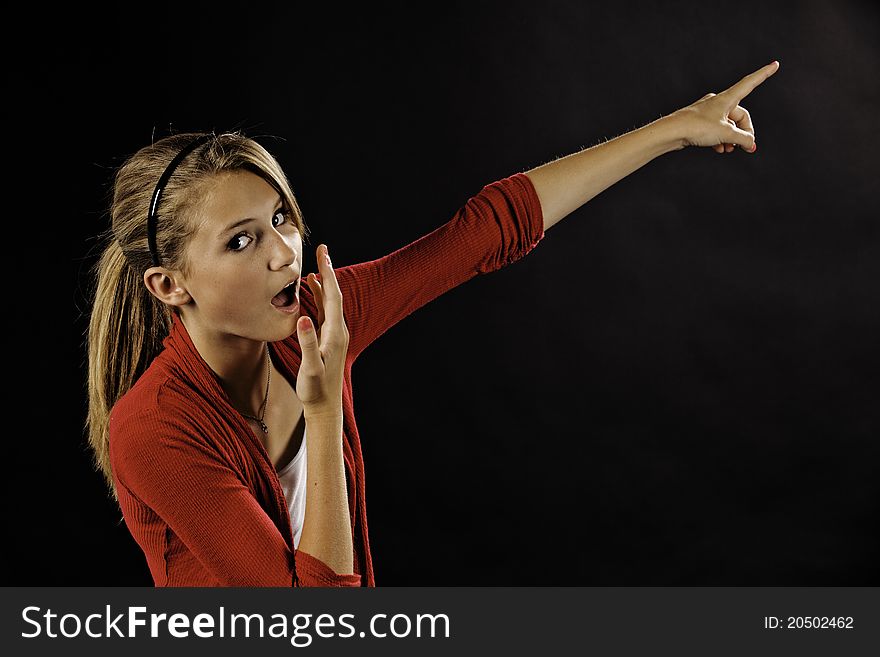 A surprised teenage female girl pointing off into the distance against a black background.