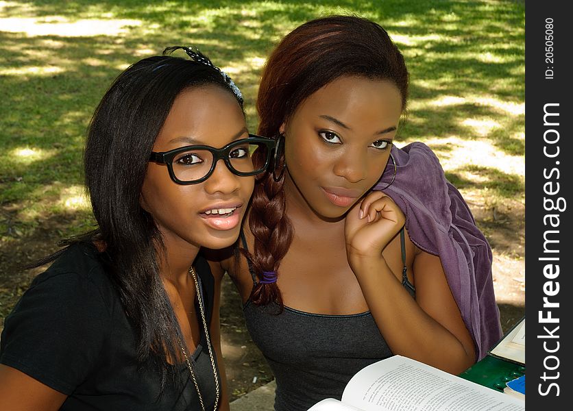 Two lovely African girls at the park, one with glasses, with an open book. Two lovely African girls at the park, one with glasses, with an open book.