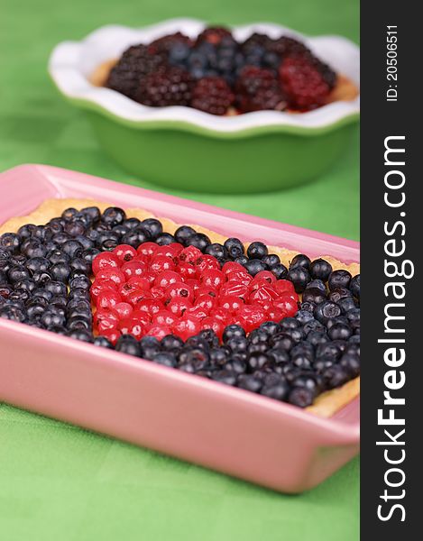 Tart with redcurrants and blueberries in a pink pottery cake tin. A tart with blueberries and raspberries out of focus in the background. Selective focus, shallow DOF. Tart with redcurrants and blueberries in a pink pottery cake tin. A tart with blueberries and raspberries out of focus in the background. Selective focus, shallow DOF.