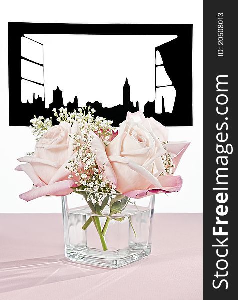 Beautiful pink roses in a square vase on a table at an open window. Window is a cut-out silhouette of a large London-like city. Table is covered with a pink cloth. Beautiful pink roses in a square vase on a table at an open window. Window is a cut-out silhouette of a large London-like city. Table is covered with a pink cloth.