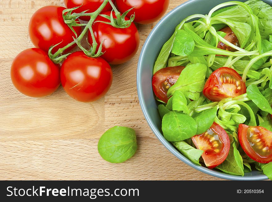 Fresh lettuce and tomatoes in a bowl, a branch of a tomato on a wooden table. Fresh lettuce and tomatoes in a bowl, a branch of a tomato on a wooden table