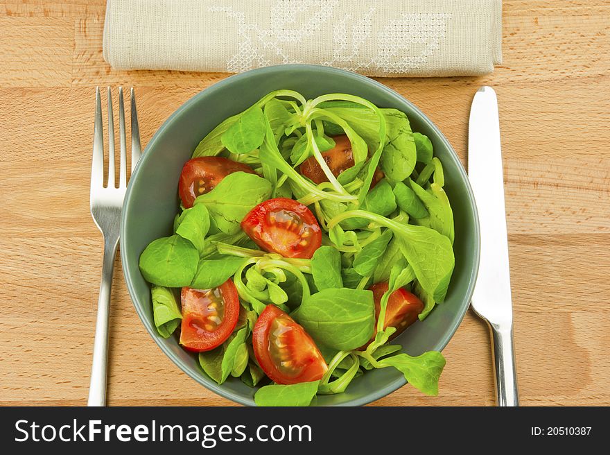 Salad of lettuce and tomatoes in a bowl, metal knife and fork, napkin linen on a wooden table. Salad of lettuce and tomatoes in a bowl, metal knife and fork, napkin linen on a wooden table