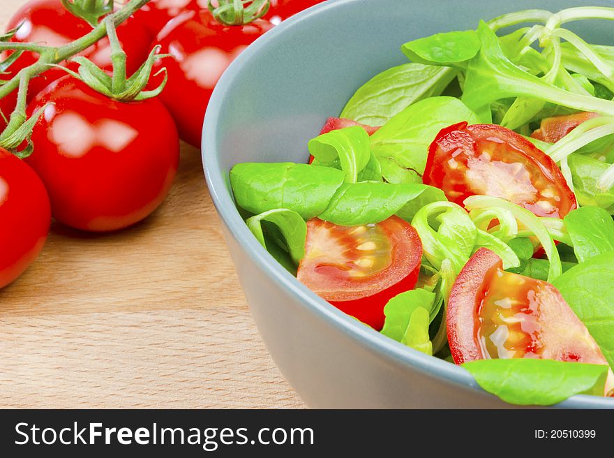 A salad of lettuce and tomatoes in a bowl with a branch of red tomatoes on a wooden table. A salad of lettuce and tomatoes in a bowl with a branch of red tomatoes on a wooden table