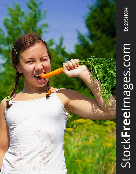 Young smiling woman bites wth effort fresh orange organic carrot in garden. Young smiling woman bites wth effort fresh orange organic carrot in garden