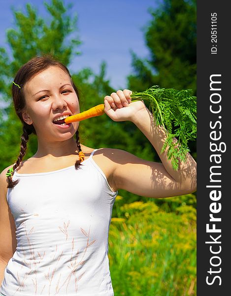 Young smiling woman holds and eats fresh orange organic carrot in garden. Young smiling woman holds and eats fresh orange organic carrot in garden