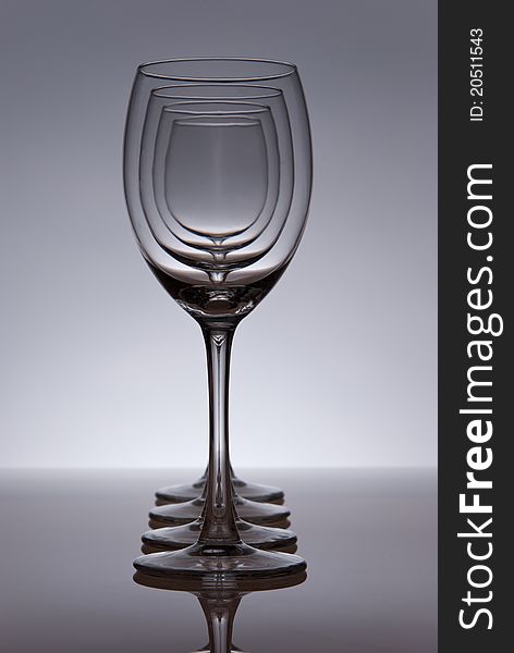 Four empty wine glasses in line. Grey table and background. Light from behind.