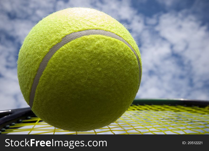 Big yellow tennis ball on racket strings outdoors a summer day. Big yellow tennis ball on racket strings outdoors a summer day.