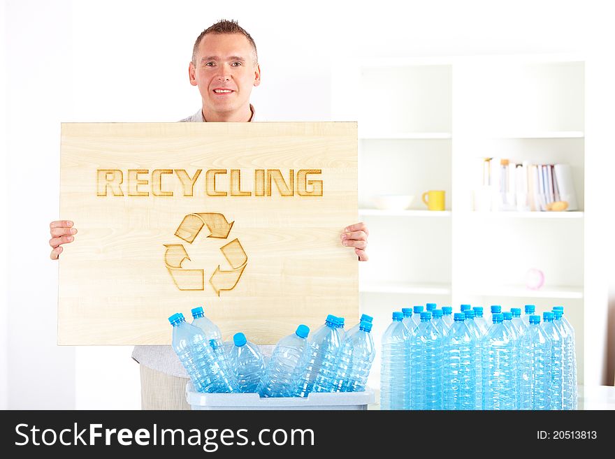 Happy man holding wooden board with word recycling and bin full of plastic blue bottles. Happy man holding wooden board with word recycling and bin full of plastic blue bottles