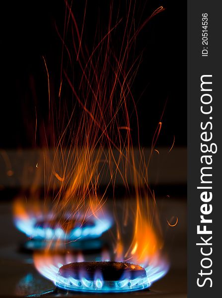 Sparks and flames above gas stove burning with blue flames