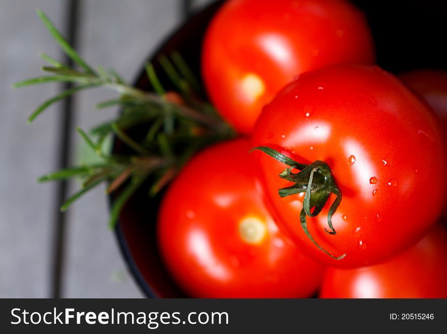 Red tomatoes in black bowl with herbs