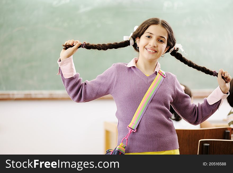 Gorgeous girl holding her hair and standing in classroom in front of board