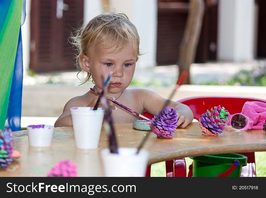 Beautiful baby girl painting beach pebbles and pine cones outdoor