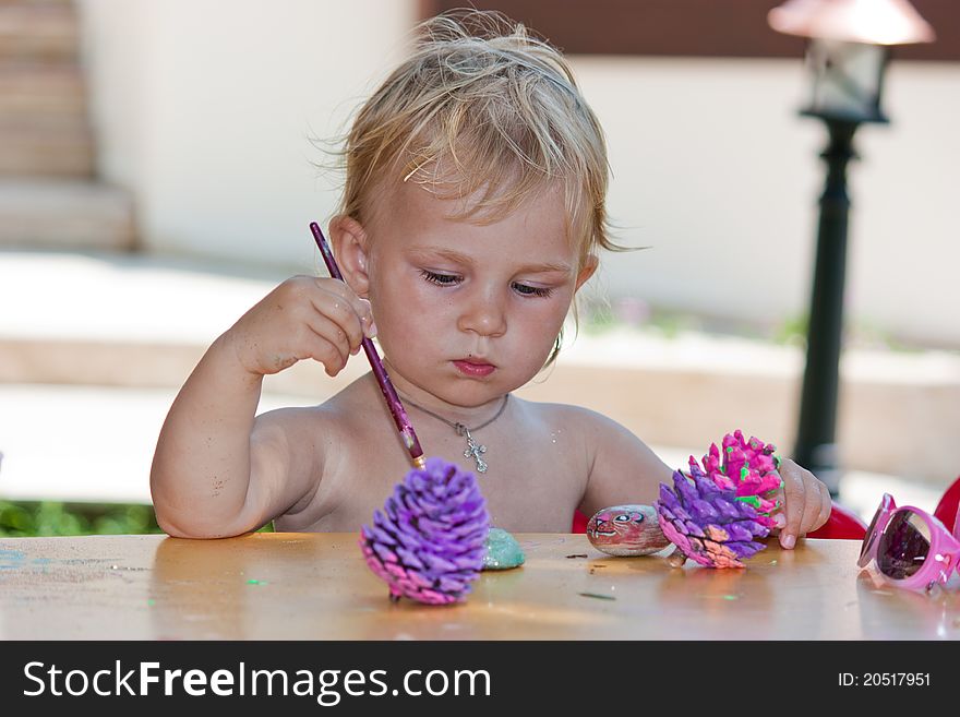 Beautiful baby girl painting beach pebbles and pine cones outdoor