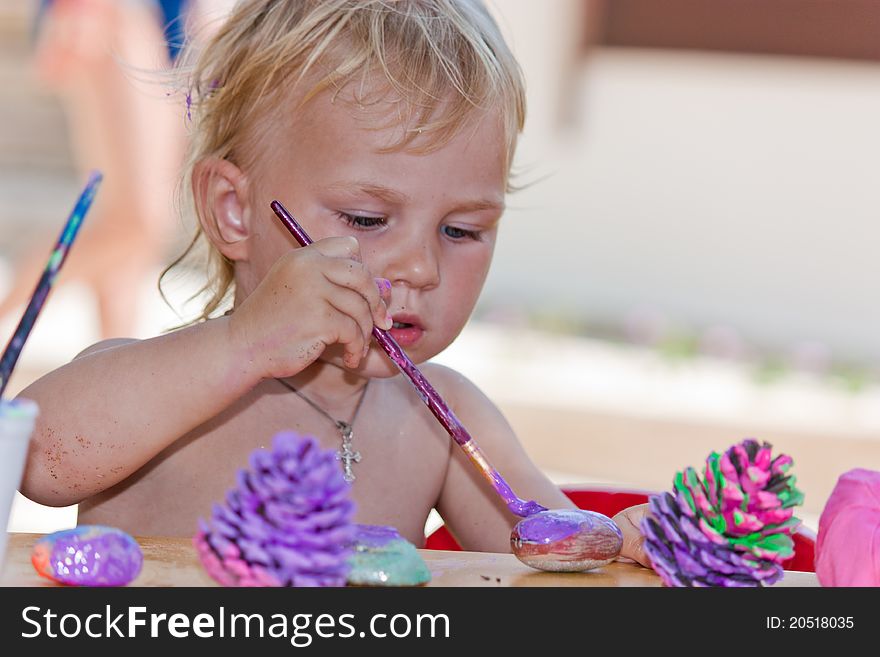 Beautiful baby girl painting beach pebbles and pine cones outdoor