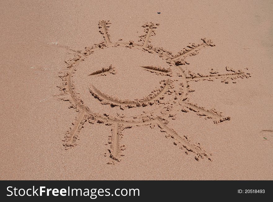 Smiling sun drawn on sand of a beach