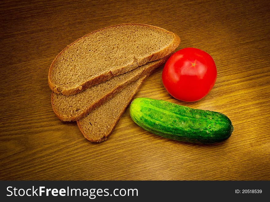 Bread, tomato and cucumber on a wooden background